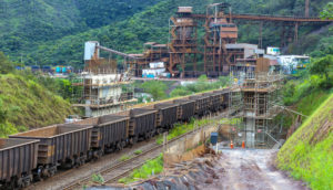 Foto de instalações de mineração com trem saindo em meio à um vale