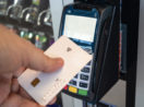 Mão de pessoa encostando cartão de crédito branco à máquina de pagamentos da Cielo