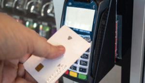 Mão de pessoa encostando cartão de crédito branco à máquina de pagamentos da Cielo