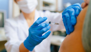 Enfermeira com luvas azuis aplicando vacina em braço de pessoa, alusivo aos serviços da CVS Health