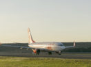 Avião da Gol Linhas Aéreas, branco com laranja, pousando em pista de aeroporto com pôr do sol