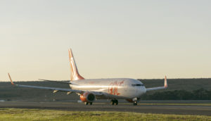 Avião da Gol Linhas Aéreas, branco com laranja, pousando em pista de aeroporto com pôr do sol