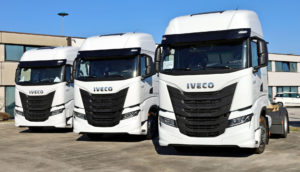 Três caminhões da Iveco lado a lado, na cor branca, em frente à concessionária da montadora