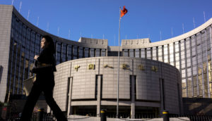 Frente do Banco do Povo da China, que reportou as reservas internacionais do país, com mulher caminhando devagar à esquerda