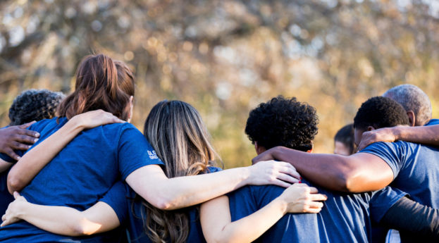 Grupo de amigos, de costas, se abraçando com camiseta azul, alusivo à benevolência