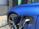 Close de mangueira de abastecimento de carros elétricos plugada à uma BMW azul marinho