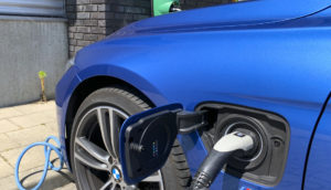 Close de mangueira de abastecimento de carros elétricos plugada à uma BMW azul marinho