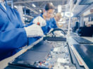 Linha de produção de produtos eletrônicos com funcionários em macacão azul, alusivo aos chips necessários à indústria