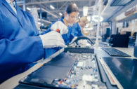Linha de produção de produtos eletrônicos com funcionários em macacão azul, alusivo aos chips necessários à indústria