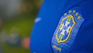 Detalhe da camisa azul da seleção brasileira, com close no escudo da CBF, alusivo aos clubes brasileiros de futebol, que tiveram lucro nos últimos 5 anos