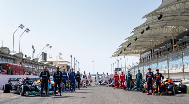 Corpo de pilotos da Fórmula (F1) reunidos na reta dos boxes de um circuito com os carros enfileirados