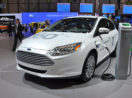 Um dos veículos elétricos da Ford, na cor branca, sendo carregado em salão de evento do setor automotivo