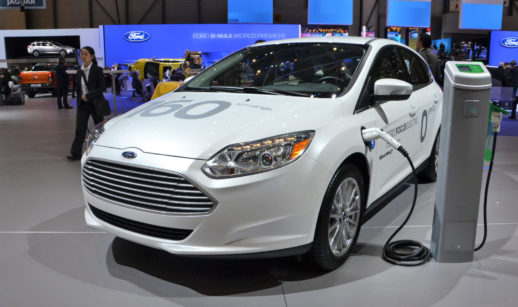 Um dos veículos elétricos da Ford, na cor branca, sendo carregado em salão de evento do setor automotivo