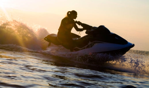 Silhueta de mulher sobre jet ski no mar com pôr do sol ao fundo