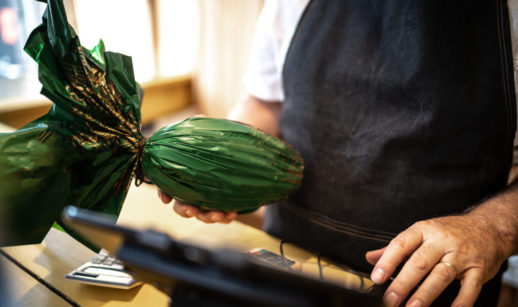 Close de vendedor com avental e ovo de Páscoa em embalagem verde, alusivo à inflação