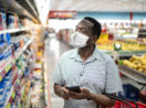 Homem usando máscara com cesta nos braços olhando produtos na prateleiro, alusivo ao IPCA de fevereiro