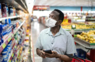 Homem usando máscara com cesta nos braços olhando produtos na prateleiro, alusivo ao IPCA de fevereiro