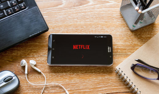 Mesa de madeira com celular ligado e logo da Netflix, criadora da série Stranger Things