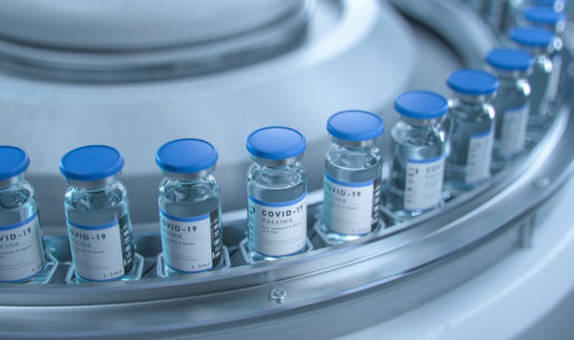 Frascos de vacinas contra a covid-19 enfileirados em máquina metálica, alusivo à Pfizer e à Moderna