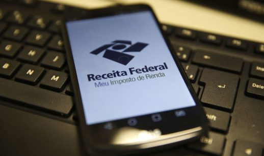 Tela de celular com o aplicativo Meu Imposto de Renda aberto, sobre teclado preto de computador, alusivo ao IRPF 2022