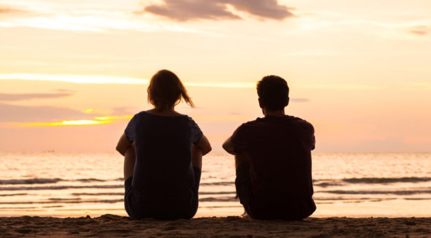 Duas pessoas sentadas de costas olhando a praia, alusivo à integração de paradoxos