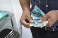 Close em mãos de homem com camisa azul e calça preta conntando notas de 100 reais, alusivo à Ume, que fornece crédito