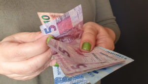 Mãos com unhas pintadas de verde contando notas de 5, 10 e 100 reais, alusivo aos valores a receber