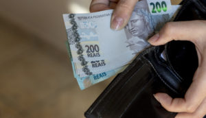 Close de mãos segurando carteira e colocando notas de 200 reais dentro, alusivo aos Valores a Receber do Banco Central