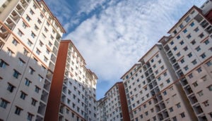 Perspectiva de baixo para cima de prédios residenciais com céu azul e nuvens brancas acima, alusivo às vendas e lançamentos de imóveis no Brasil