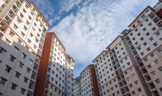 Perspectiva de baixo para cima de prédios residenciais com céu azul e nuvens brancas acima, alusivo às vendas e lançamentos de imóveis no Brasil
