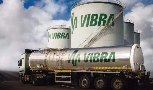 Caminhão tanque da Vibra Energia, com destaque para o logo em verde, e tonéis gigantes ao fundo, alusivo aos resultados do 4º trimestre da companhia
