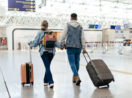 Um homem e uma mulher andam por um aeroporto com suas malas, em alusão a uma viagem de férias