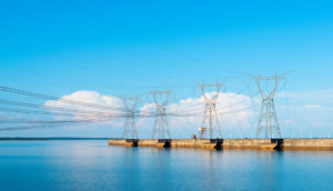 Torres de transmissão de energia com céu e rio azuis, alusivo às ações do setor com foco em dividendos para abril