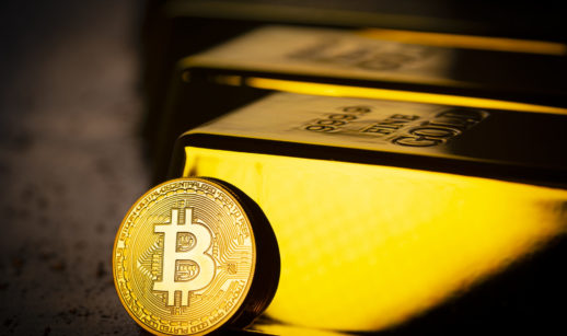 Foto conceitual de moeda alusivo ao Bitcoin encostada em barra de ouro reluzente