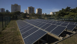 Painéis de energia solar no Brasil enfileirados em gramado com prédios iluminados ao fundo