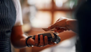Close de pessoa aproximando o cartão de crédito a uma máquina de pagamento, alusivo ao financiamento