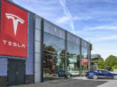 Fachada de concessionária da Tesla, cujas ações foram vendidas por Elon Musk, com destaque para vidros e carro parado na entrada e logo gigante da empresa