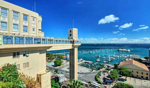 Vista do elevador da cidade de Salvador, na Bahia, com céu azul e barcos atracados próximos, alusivo ao turismo no Brasil
