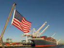 Bandeira dos Estados Unidos em primeiro plano com navio cargueiro ao fundo, alusivo às commodites que ganharam espaço na carteira de BDRs de maio do Safra