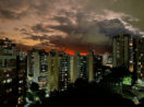 Pôr do sol alaranjado com prédios na frente e árvores escurecidos abaixo, alusivo ao valor do aluguel no Brasil