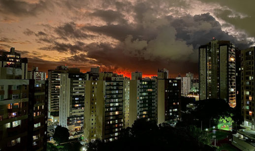 Pôr do sol alaranjado com prédios na frente e árvores escurecidos abaixo, alusivo ao valor do aluguel no Brasil