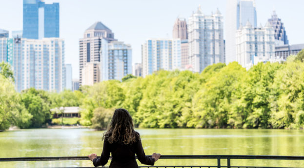 Mulher de costas em ponte olhando para árvores em parque com prédios ao fundo, alusivo às práticas ESG