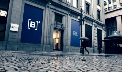 Fachada da B3, bolsa de valores brasileira, em dia chuvoso com gente passando com guarda-chuva em frente, alusivo à queda em junho
