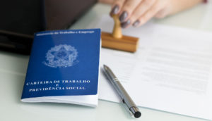 Carteira de Trabalho azul sobre mesa com papéis e carimbo, alusivo aos empregos formais no Brasil em abril