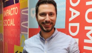 Felipe Oliva, CEO da Squid, sorrindo, de camisa branca com mural atrás colorido