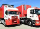 Dois caminhões da JSL (JSLG3) em vermelho e branco, lado a lado, estacionados, com céu azul atrás