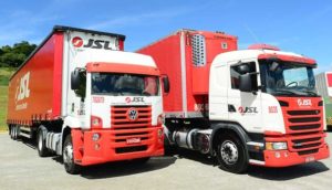 Dois caminhões da JSL (JSLG3) em vermelho e branco, lado a lado, estacionados, com céu azul atrás