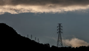 Torres de transmissão de energia elétrica em cima de morro com céu escurecido, alusivo à Light