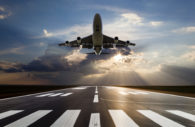 Perspectiva de baixo para cima de avião decolando em aeroporto com sol atrás, alusivo ao setor aéreo