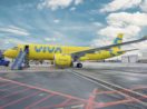 Avião amarelo da companhia low cost Viva parado em aeroporto com céu azul